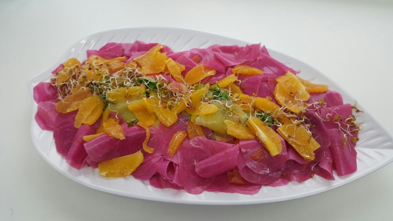 Świąteczna sałatka z marynowanych buraków, pomarańczy i kiełków na białym talerzu w kształcie liścia.