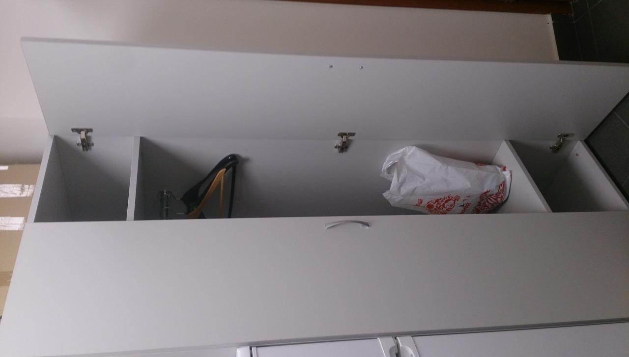 Wnętrze białej szafki z otwartymi drzwiczkami, widoczne przegródki z damskimi butami na obcasie i reklamówką ze wzorem.