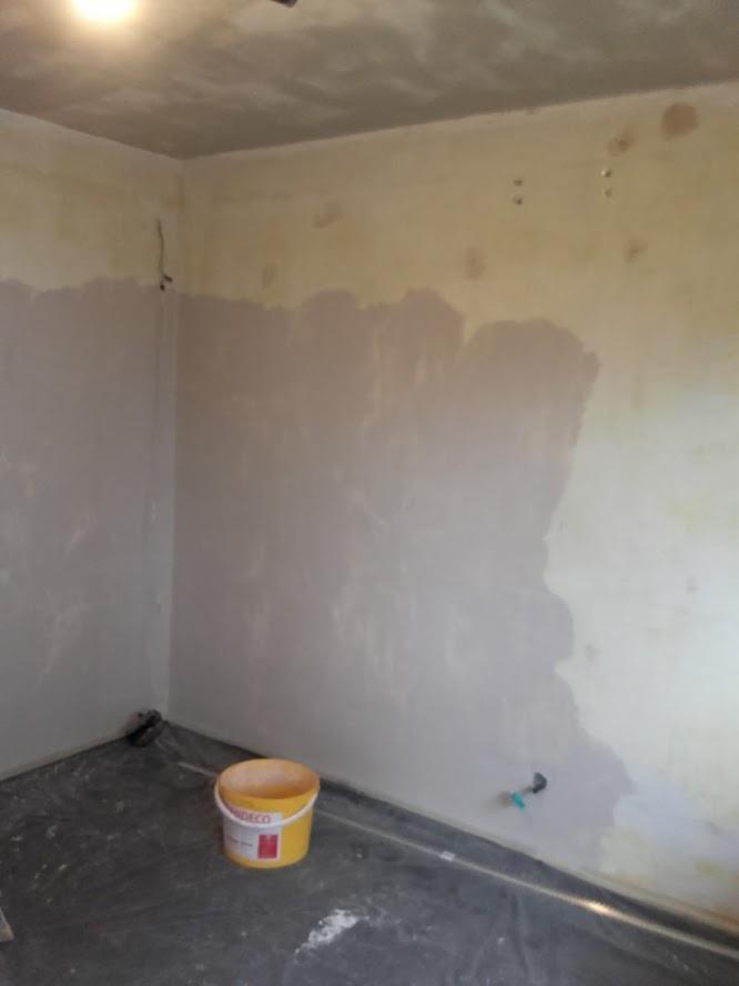 Pokój w trakcie prac wykończeniowych, ściany częściowo pokryte gładzią szpachlową, wiadro z masą szpachlową na podłodze zabezpieczonej folią.