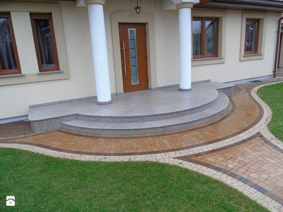 Wejście do domu z granitowymi schodami i ścieżką z kostki brukowej w odcieniach brązu, otoczone trawnikiem.