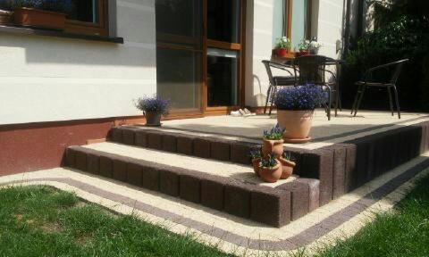 Schody wejściowe do domu wyłożone kostką brukową w odcieniach brązu i beżu, z doniczkami z lawendą na stopniach, prowadzące na taras z meblami ogrodowymi.