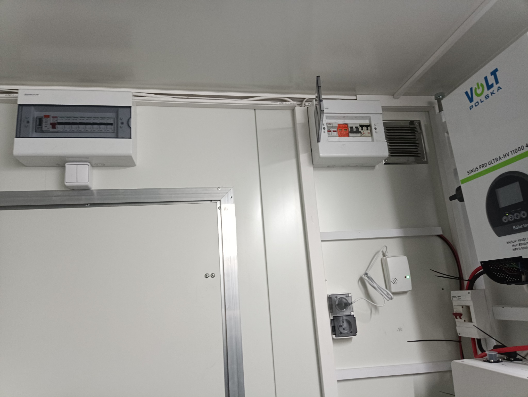 Białe wnętrze kontenera z zamontowanymi dwoma rozdzielnicami elektrycznymi, gniazdkami i panelem sterowania Volt Polska Sinus Pro Ultra-HV 11000 48V.