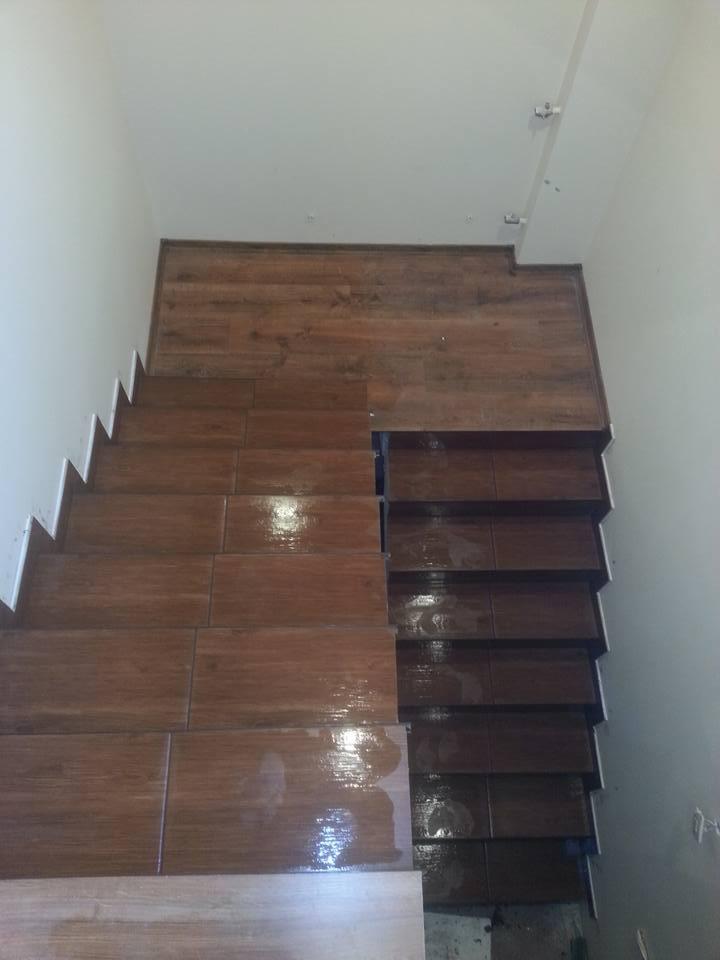 Schody wyłożone brązowymi płytkami imitującymi drewno, widok z góry, widoczne niedokończone fragmenty.