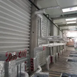 Widok instalacji wentylacyjnej z izolowanymi kanałami w budynku komercyjnym, widoczne elementy montażowe i konstrukcja stropu.