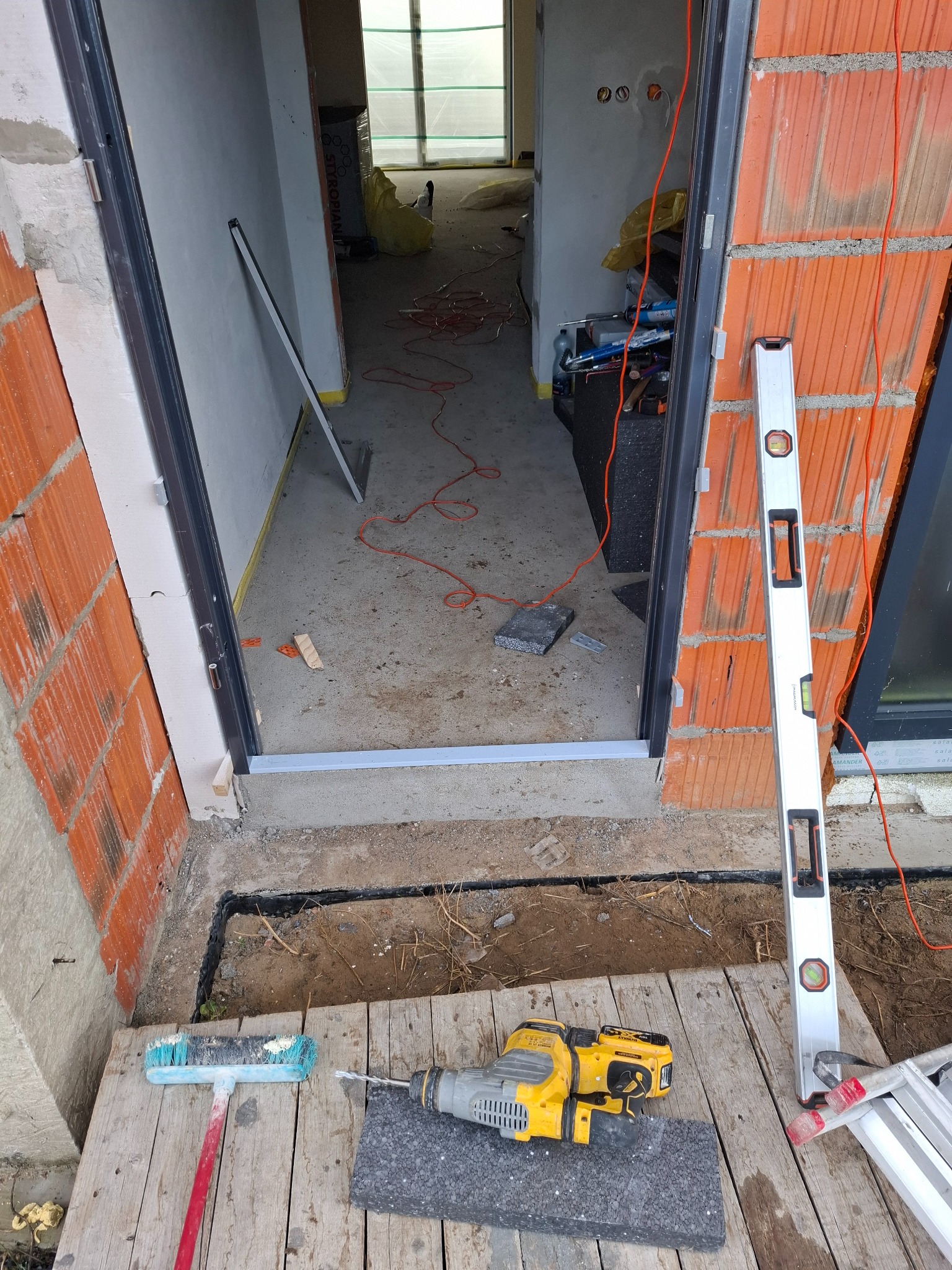 Montaż ościeżnicy w surowym otworze drzwiowym z użyciem poziomicy, widoczne narzędzia i materiały budowlane w pomieszczeniu w trakcie prac wykończeniowych.