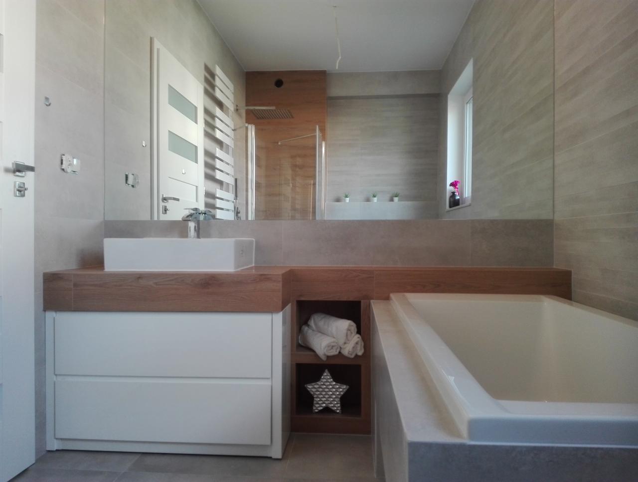 Jasna łazienka z wanną, umywalką nablatową i dużym lustrem, wykończona płytkami w odcieniach szarości, z elementami drewnianymi i dekoracyjną gwiazdą w półce.