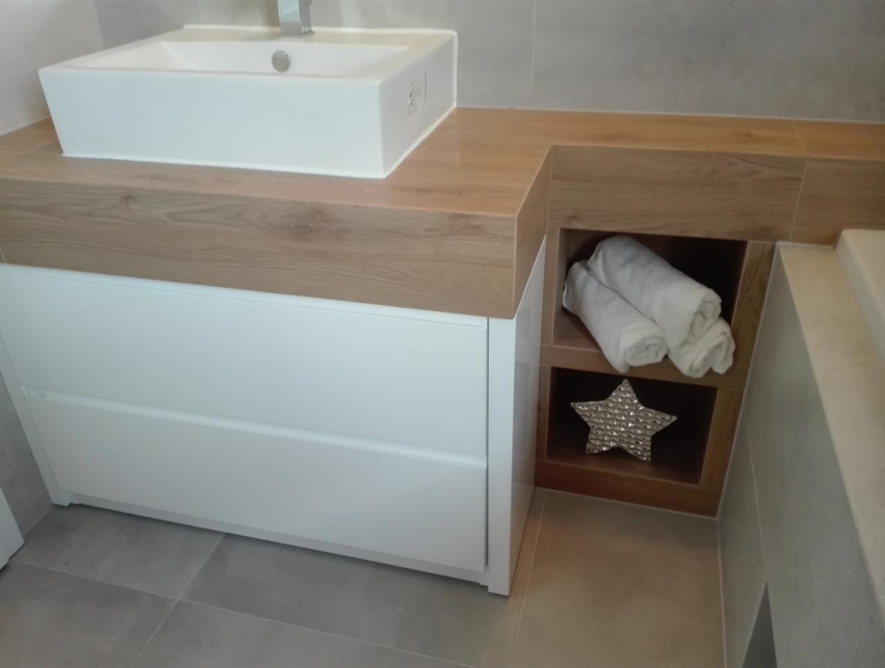 Nowoczesna łazienka z białą, prostokątną umywalką nablatową, drewnianym blatem, białymi szufladami i półką z ręcznikami oraz dekoracyjną gwiazdą.