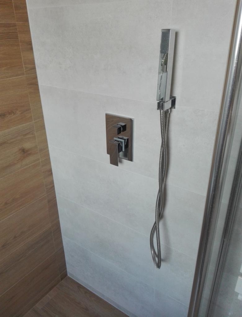 Nowoczesna kabina prysznicowa z chromowaną armaturą i deszczownicą, wykończona płytkami w odcieniach bieli i drewna.