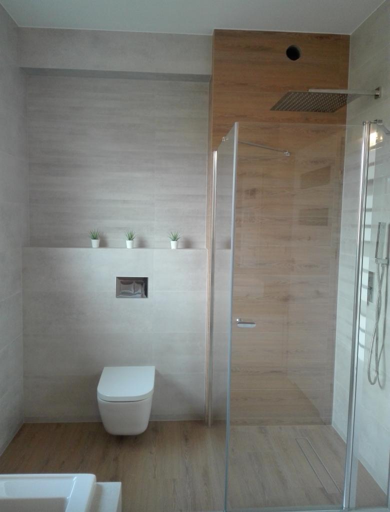 Nowoczesna łazienka w Bolesławcu z kabiną prysznicową typu walk-in, podwieszaną toaletą i drewnopodobnymi płytkami na podłodze i części ściany.