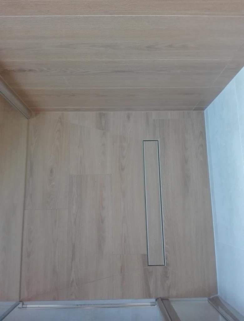 Wykończona łazienka z drewnopodobną podłogą i odpływem liniowym w kabinie prysznicowej, widok z góry.