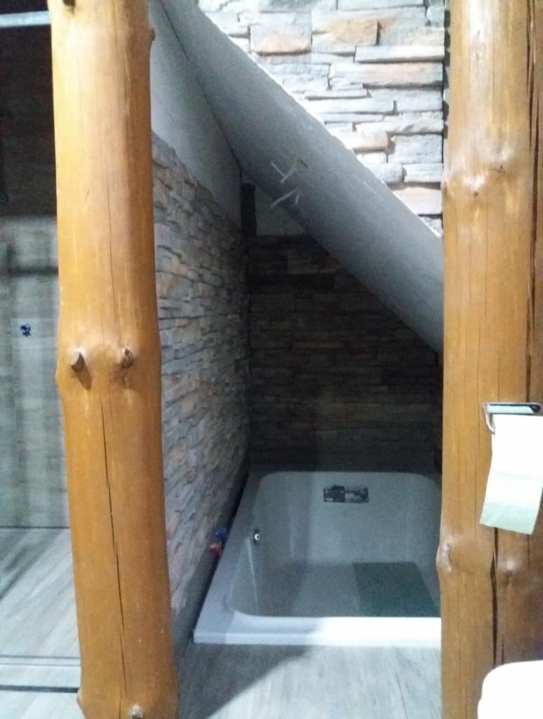 Nowoczesna łazienka z wanną w zabudowie, wykończona kamieniem dekoracyjnym i drewnianymi belkami, widok na narożną wannę z hydromasażem w skosie poddasza.