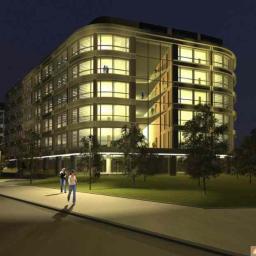 Property Investment sp zo.o. - Nowoczesny budynek biurowy z zaokrąglonymi narożnikami, oświetlony nocą, z widocznymi osobami wewnątrz, otoczony zielenią i chodnikiem.