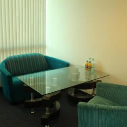 Property Investment sp zo.o. - Nowoczesny pokój biurowy z turkusowymi fotelami w paski, szklanym stołem z napojami i żaluzjami w tle.