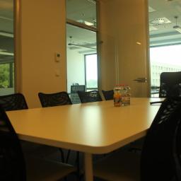 Property Investment sp zo.o. - Sala konferencyjna w Szczecinie z białym stołem, czarnymi krzesłami z siatki i napojami na stole, widok przez szklane drzwi na biurowiec.