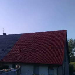 Dom z dwoma rodzajami pokrycia dachowego: szarym i czerwonym, widoczne kominki wentylacyjne na czerwonej części, antena satelitarna na szarej.