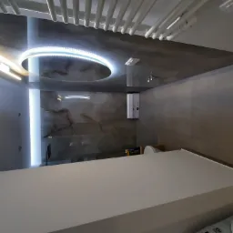 Nowoczesna łazienka z podświetlanym sufitem, imitacją marmuru na ścianach i minimalistyczną umywalką.