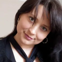 Portret uśmiechniętej prawniczki z ciemnymi włosami, w czarnej bluzce z wiązanym dekoltem i złotymi kolczykami, patrzącej w obiektyw.