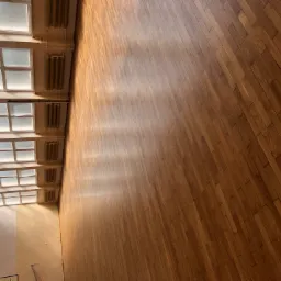 Wycyklinowana podłoga parkietowa w hali sportowej, widoczne okna dachowe i grzejniki żeliwne.