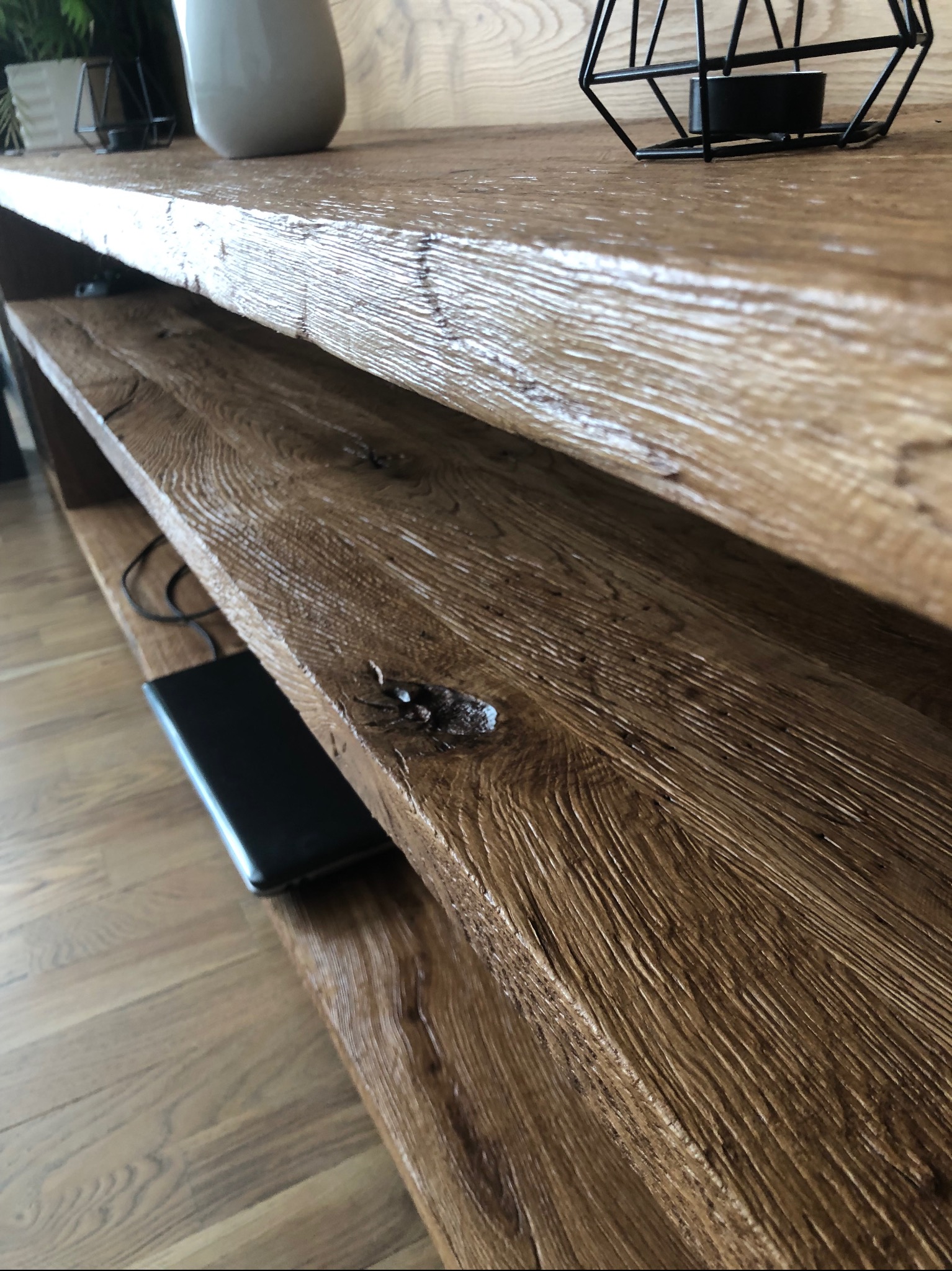 Ręcznie wykonana, drewniana półka z wyraźnym usłojeniem i sękami, wykończona lakierem. Na półce dekoracje i elektronika. Widoczna struktura drewna i detale wykończenia.