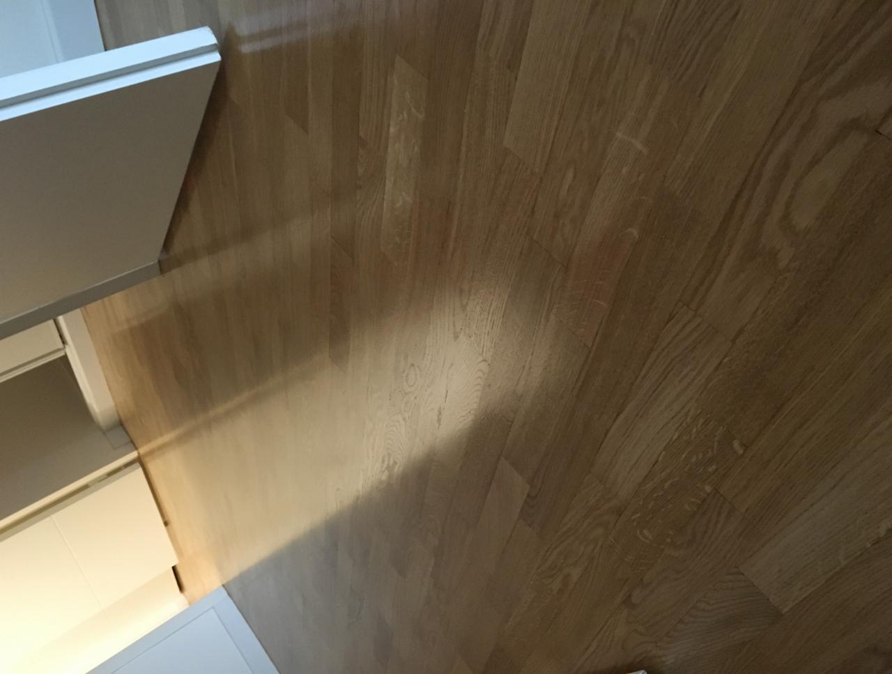 Jasny, lakierowany parkiet z widoczną strukturą drewna, częściowo oświetlony, przylegający do białych mebli.