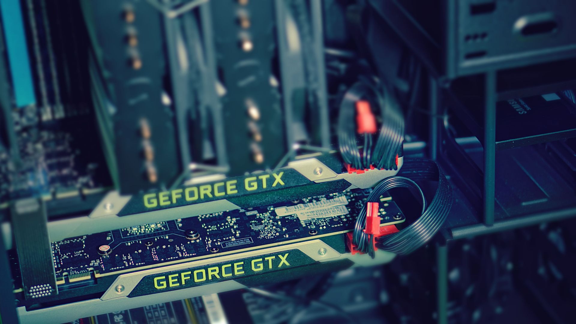 Dwie karty graficzne GeForce GTX zainstalowane wewnątrz obudowy komputera, z widocznymi kablami zasilającymi i elementami płyty głównej w tle.