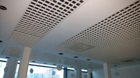 Biały sufit podwieszany z kratownicą w biurze, widoczne elementy wentylacji i oświetlenia, z perspektywy dolnej.