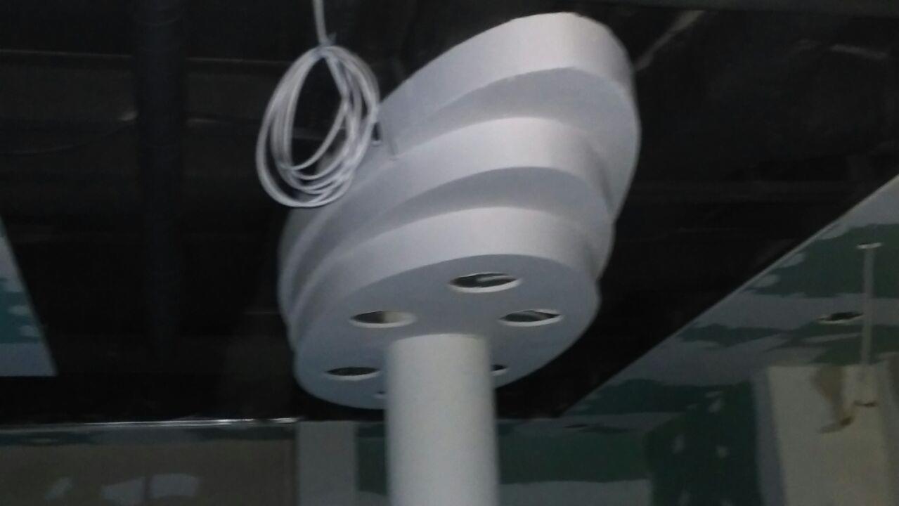 Niedokończona konstrukcja sufitowa z okrągłymi elementami i otworami, widoczne przewody elektryczne i surowy stan wykończenia pomieszczenia.