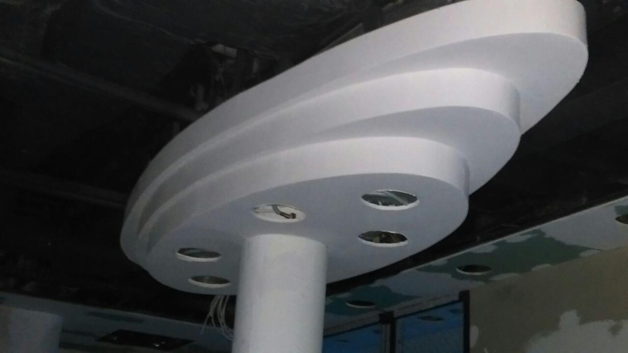 Nietypowa, trójstopniowa, owalna konstrukcja sufitowa w kolorze białym z otworami na oświetlenie, zamontowana w pomieszczeniu w trakcie wykończenia.