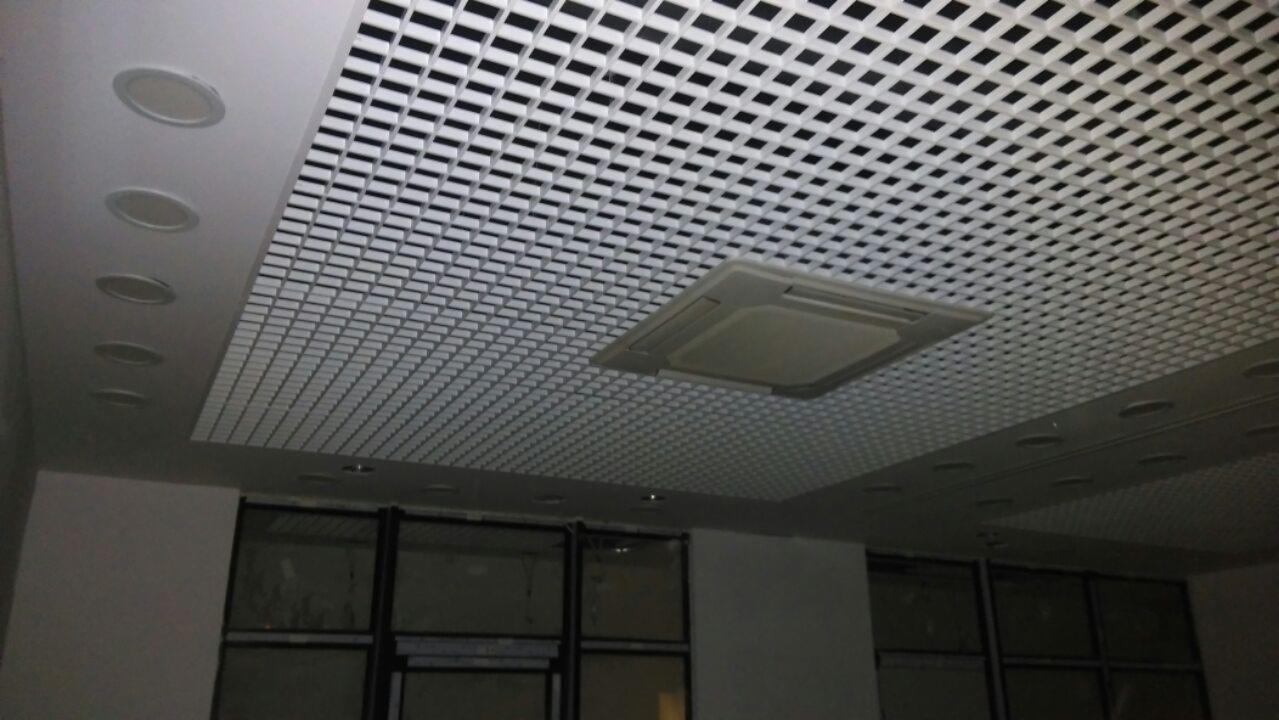 Kasetonowy sufit podwieszany z kratownicą w biurze, z wbudowanymi okrągłymi lampami i centralną klimatyzacją.