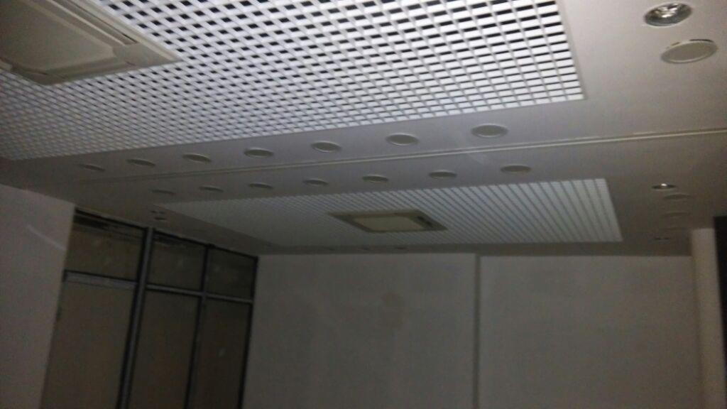 Sufit podwieszany z kratownicą, oświetleniem punktowym i klimatyzacją w biurze, widok z dołu, z fragmentem ściany i przeszklonymi drzwiami.