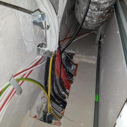 MichaelAngelo Interiors With Passion ANDRZEJ NOWAK - Instalacja elektryczna w trakcie remontu: widoczne kable w kolorowych izolacjach, metalowe uchwyty mocujące, fragment wentylacji z folii aluminiowej i profil konstrukcji ściany działowej.