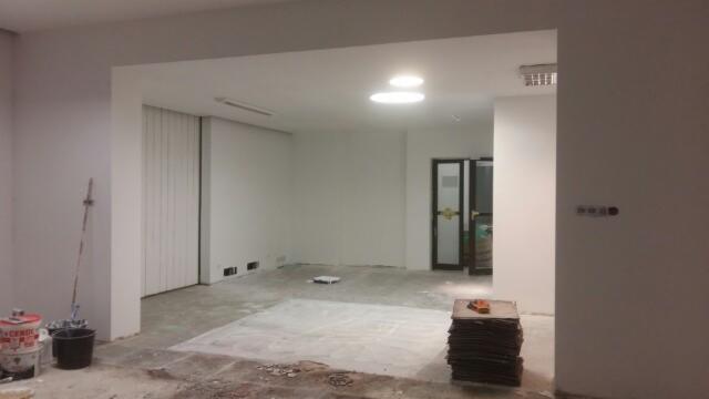 Wnętrze biura w trakcie prac wykończeniowych: widoczne przygotowane płytki na podłodze, ściany po malowaniu, przygotowane narzędzia malarskie i zaklejona folią brama.