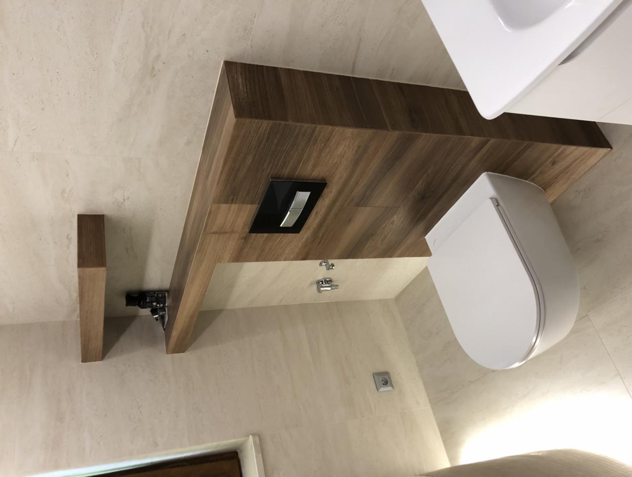 Nowoczesna toaleta podwieszana z drewnianym blatem i ukrytym systemem spłukiwania, widoczne elementy montażowe i marmurowe płytki na ścianie.