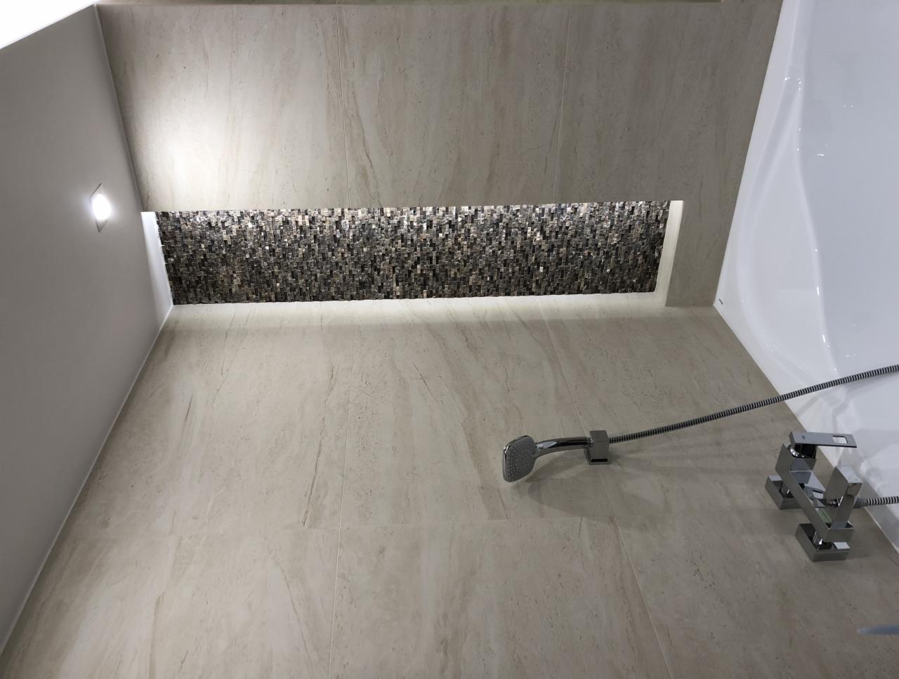 Wykończona łazienka z beżowymi płytkami imitującymi marmur, mozaiką wnękową i nowoczesną chromowaną armaturą.