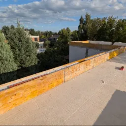 Wylana płyta betonowa stropu z szalunkiem i widokiem na zieleń. Elementy konstrukcyjne budynku w trakcie budowy. Słoneczny dzień.