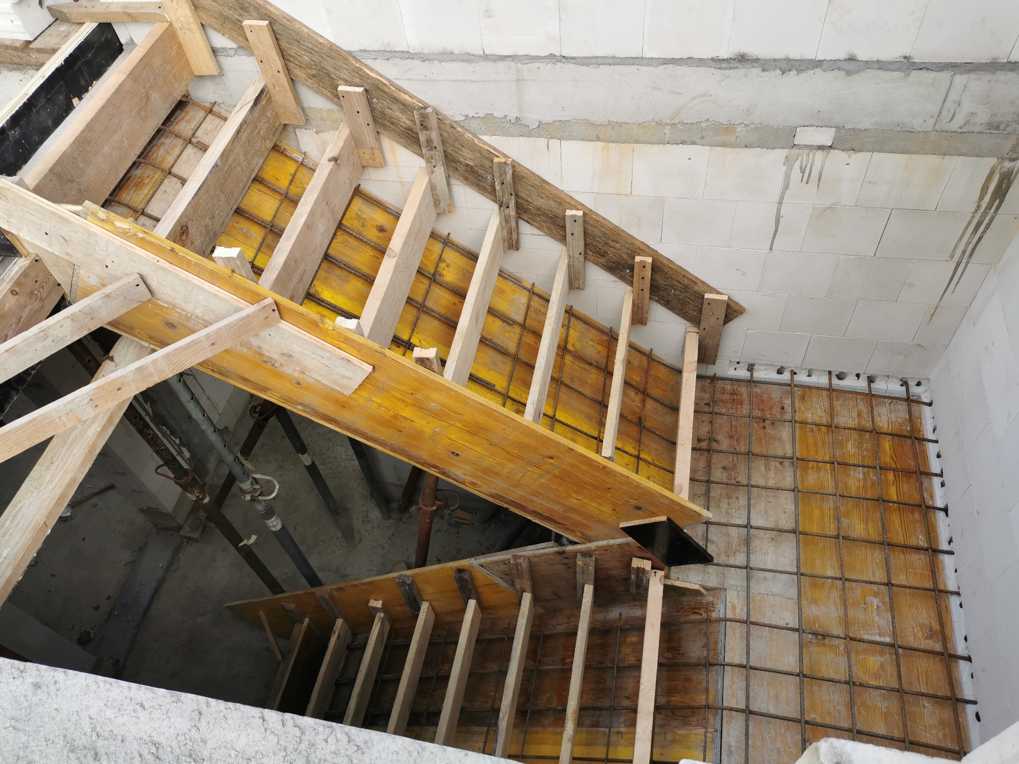 Wewnętrzny widok na szalunek drewniany i zbrojenie przygotowane pod betonowe schody w surowym stanie budynku.