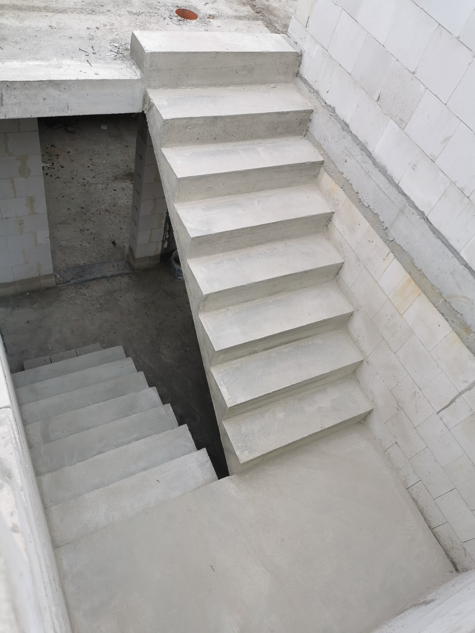 Surowe, betonowe schody wewnętrzne w trakcie budowy, widok z góry, z widocznymi bloczkami z betonu komórkowego po bokach.