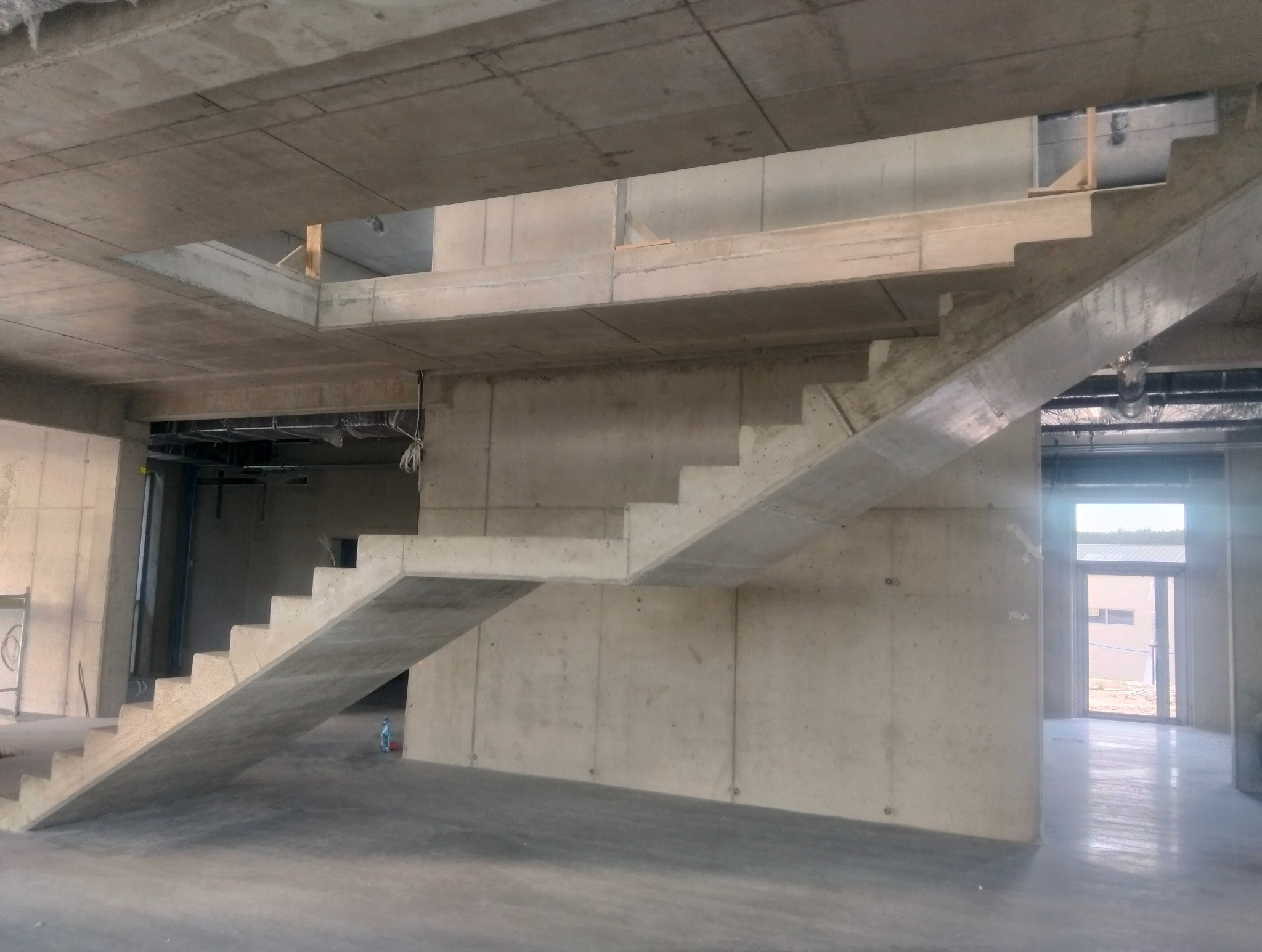 Surowe, betonowe schody w budynku w trakcie budowy. Widoczne ściany i sufit również z betonu, podkreślające minimalistyczny, industrialny charakter wnętrza.
