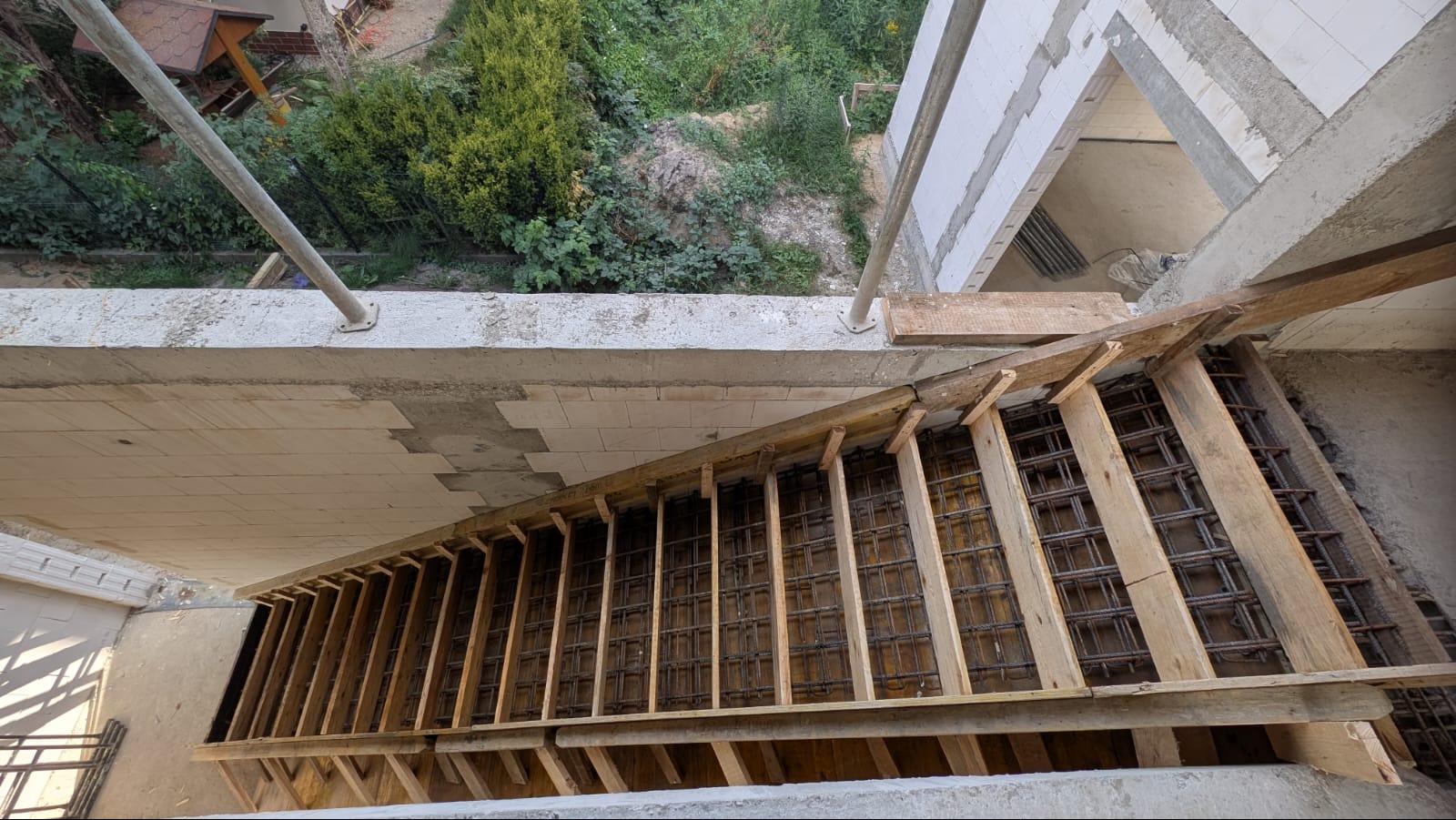 Betonowe schody w trakcie budowy: drewniane szalunki zbrojone stalą, widok z góry. Elementy konstrukcyjne z betonu komórkowego w tle, zieleń na zewnątrz.
