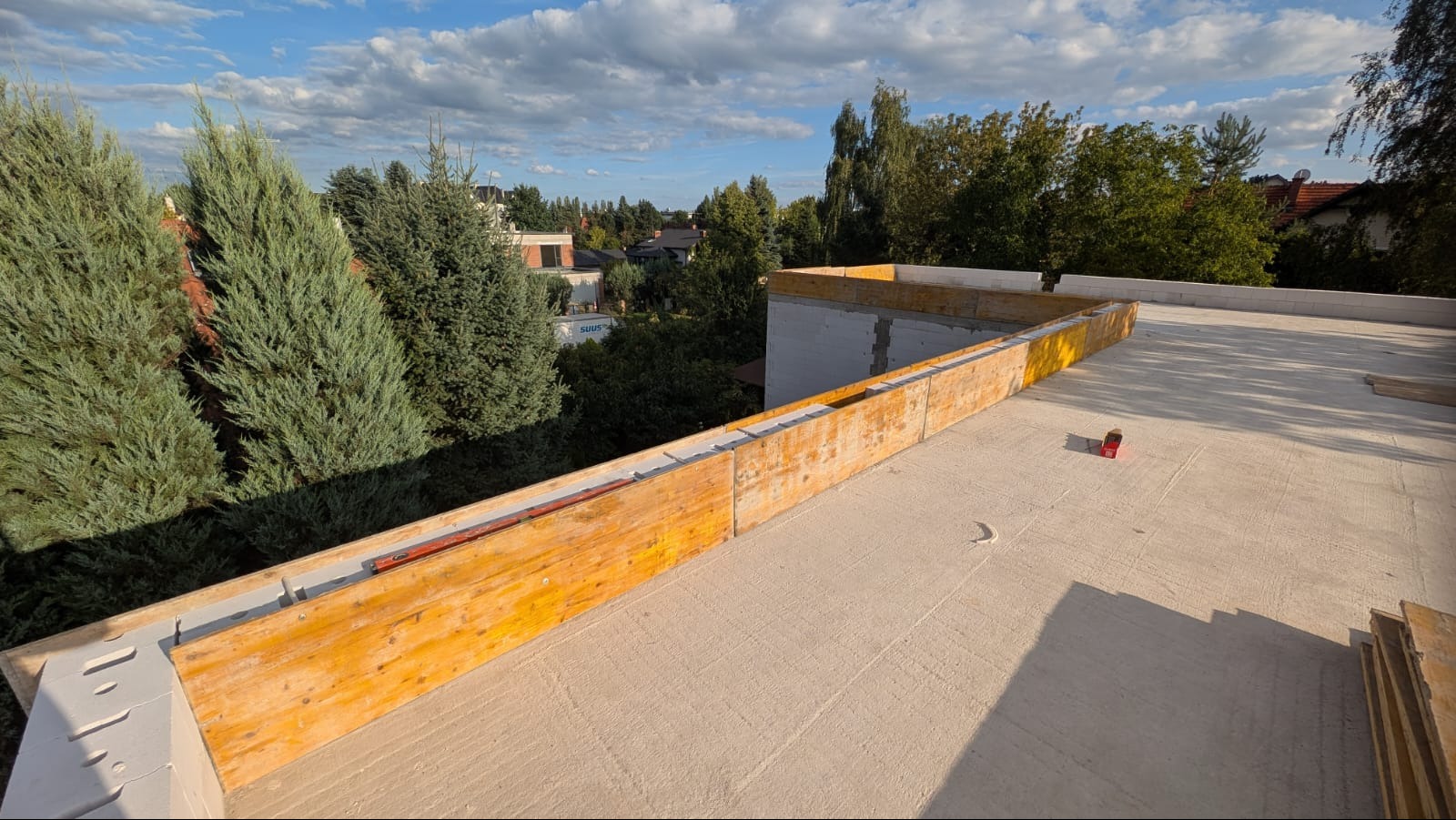 Wylana płyta betonowa stropu z szalunkiem i widokiem na zieleń. Elementy konstrukcyjne budynku w trakcie budowy. Słoneczny dzień.