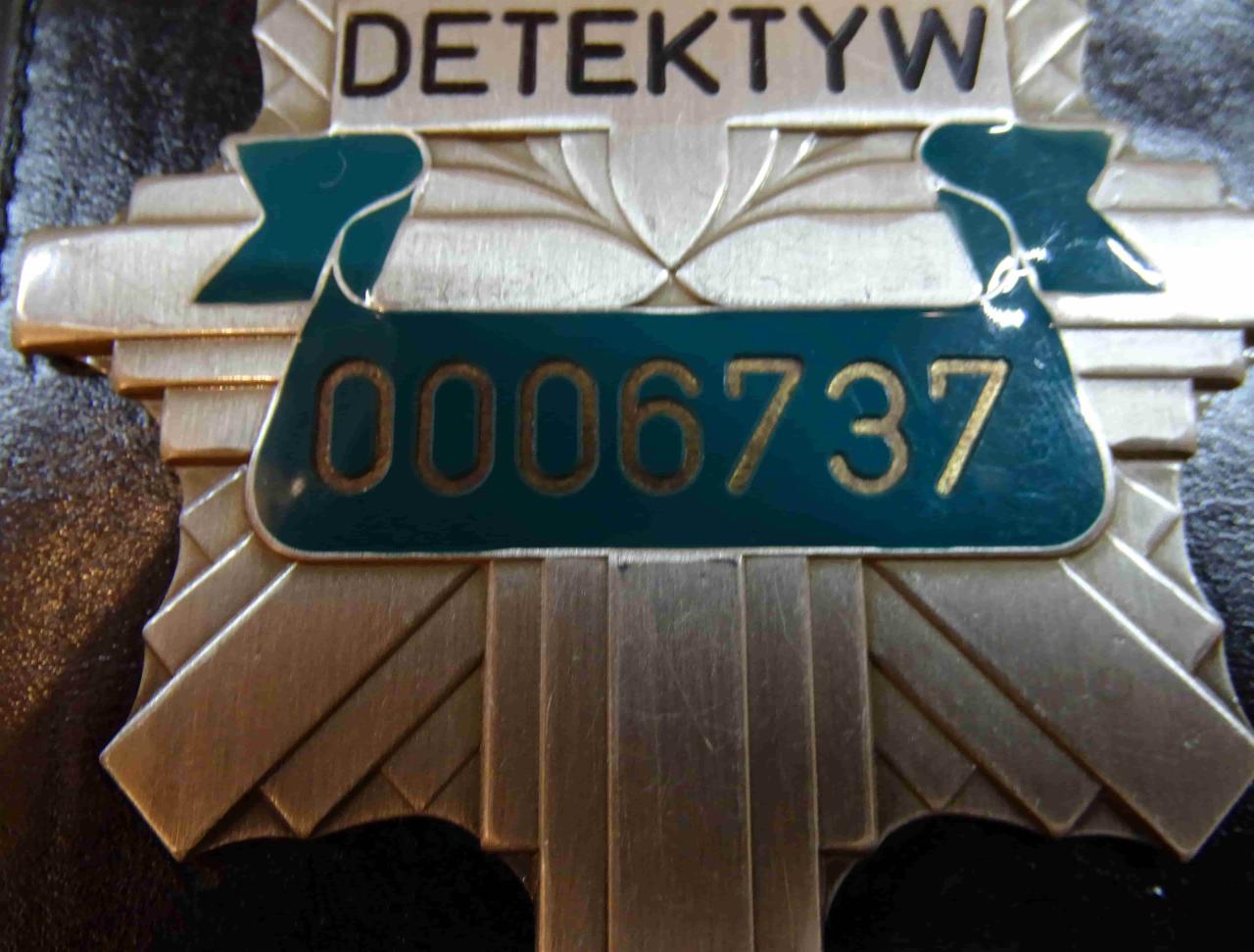 Metalowa odznaka z napisem i numerem identyfikacyjnym na ciemnym tle.