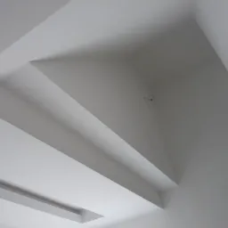 Biały sufit z wielopoziomową konstrukcją z płyt gipsowo-kartonowych i wnęką na oświetlenie, widok z dołu.