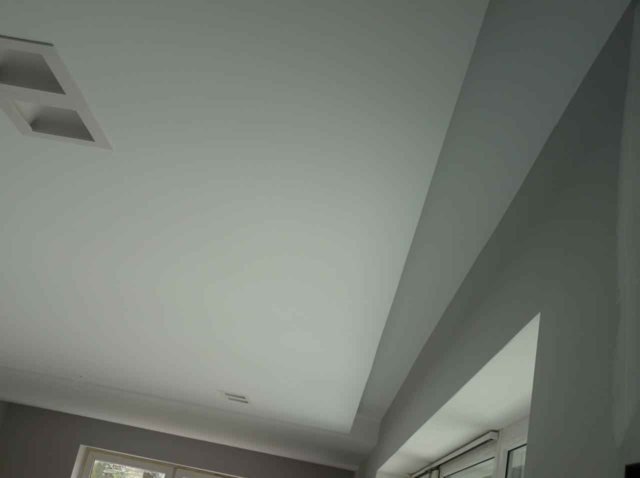Wykończony sufit podwieszany z płyt karton gips z wbudowanym oświetleniem punktowym, widok z dołu pod kątem, ściana pomalowana na szaro.