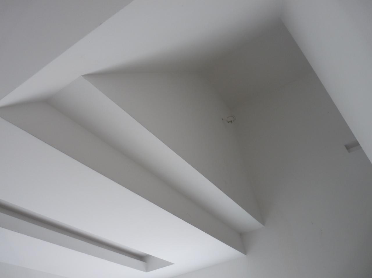 Biały sufit z wielopoziomową konstrukcją z płyt gipsowo-kartonowych i wnęką na oświetlenie, widok z dołu.