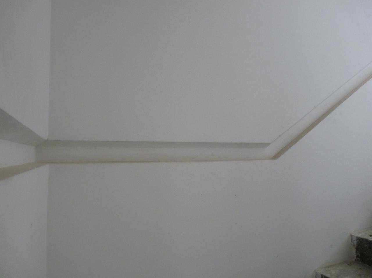 Szara ściana z listwą dekoracyjną biegnącą wzdłuż sufitu i schodami w prawym dolnym rogu.