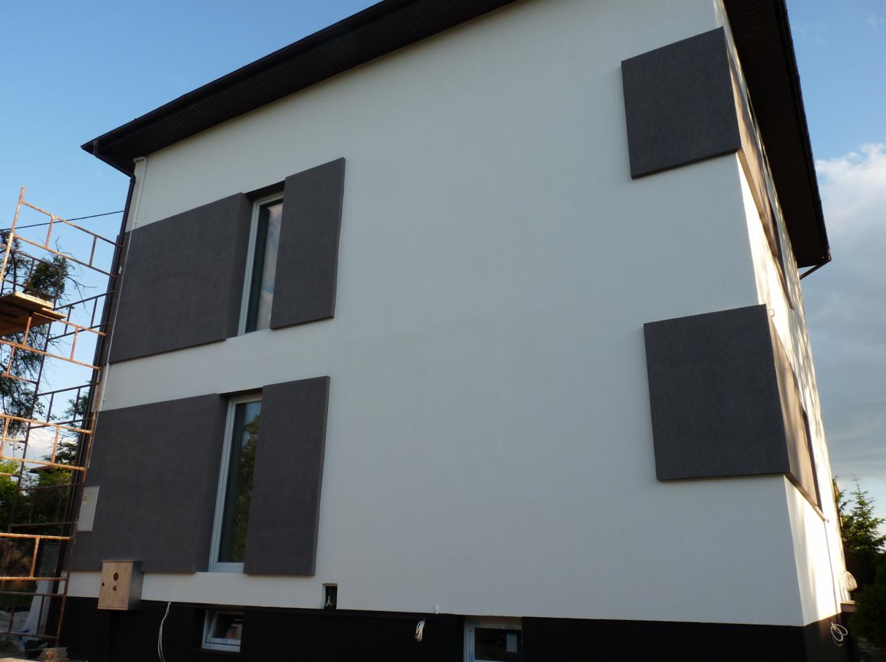 Elewacja budynku z zamontowanymi szarymi panelami elewacyjnymi, widoczne rusztowanie z lewej strony budynku.