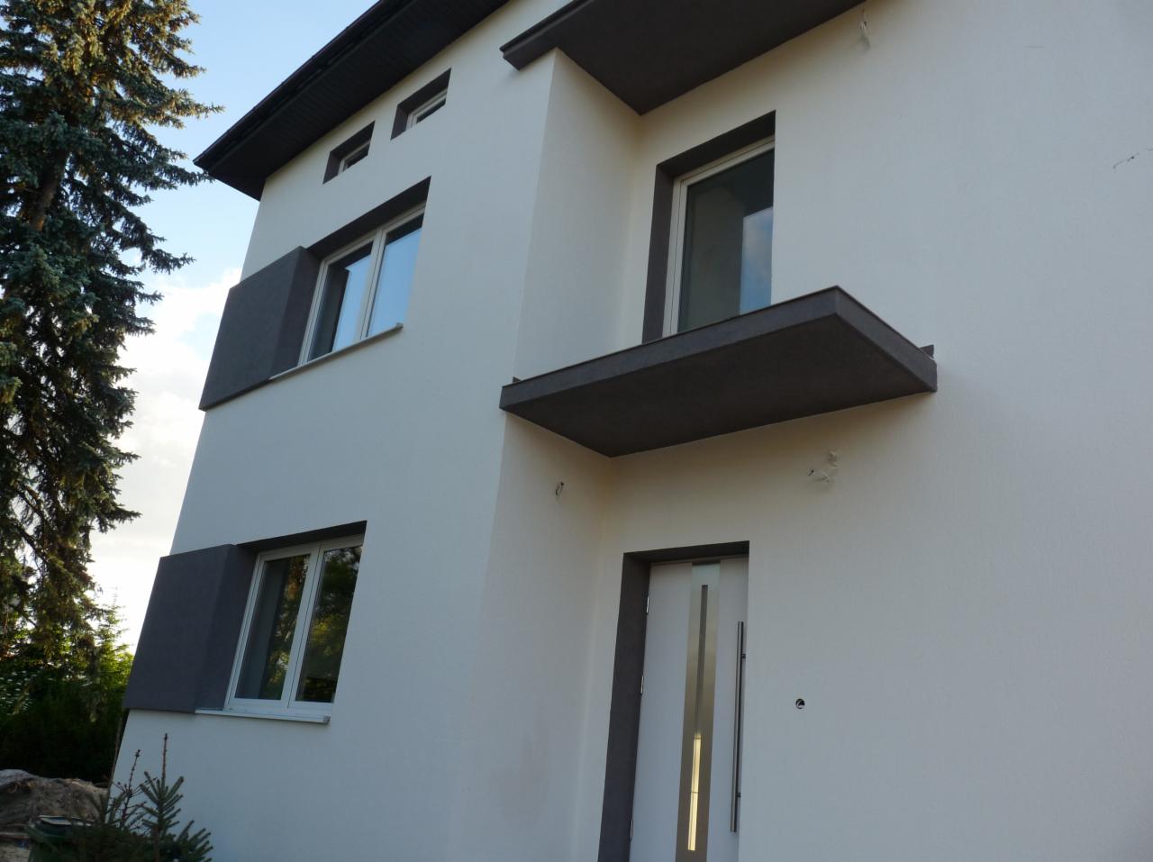 Nowoczesny dom dwupiętrowy z białymi ścianami, szarymi elementami dekoracyjnymi i minimalistycznym balkonem, widok z dołu.