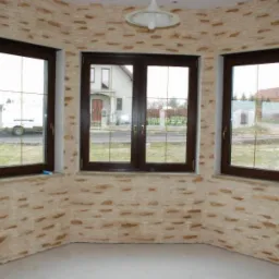 Pokój w Kożuchowie z trzema oknami i ścianami wykończonymi dekoracyjnym kamieniem w odcieniach beżu i brązu, widoczne elementy roweru i lampa sufitowa.