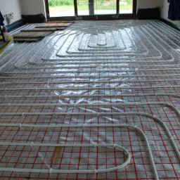 Rozłożona instalacja ogrzewania podłogowego na folii z czerwoną siatką, przed wylaniem wylewki, widoczne białe rurki ułożone w pętle.