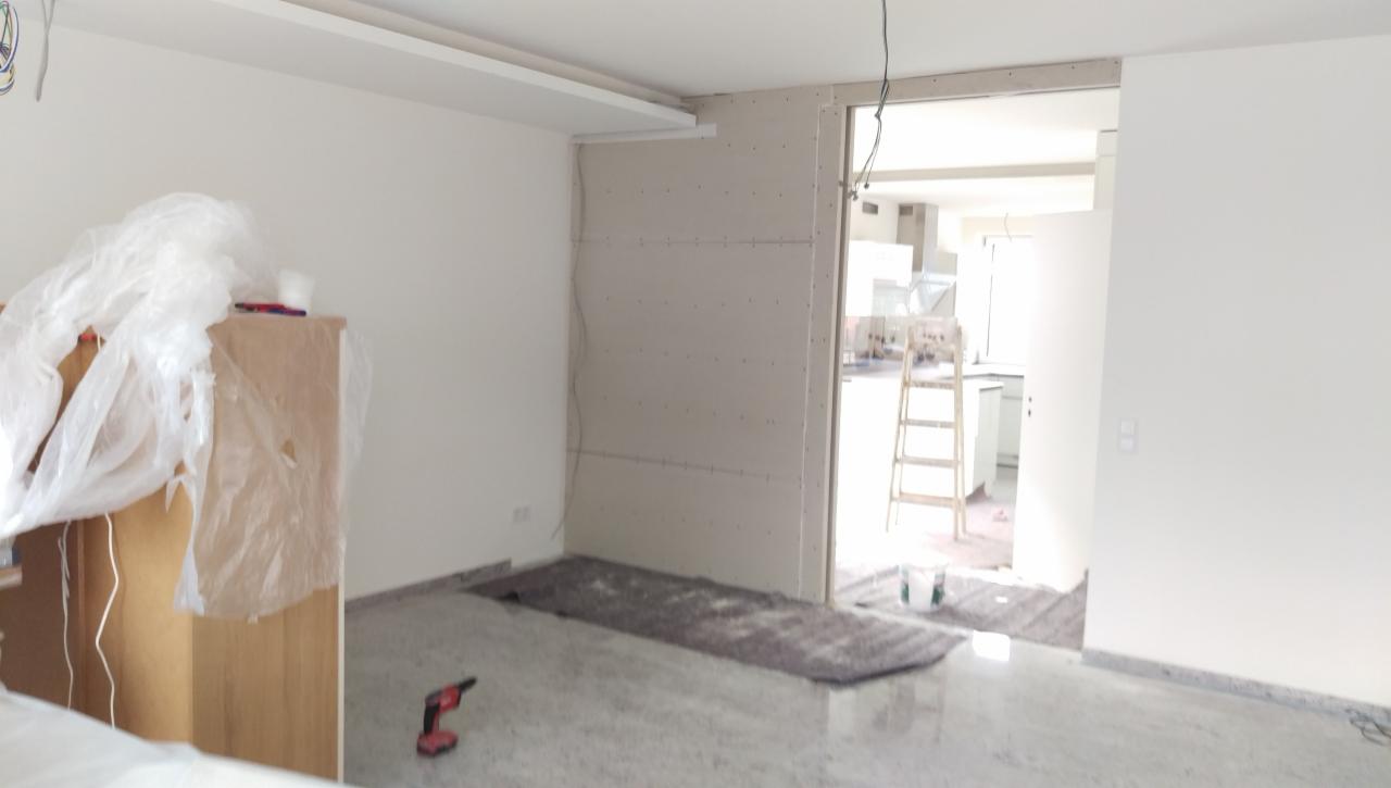 Pokój w trakcie prac wykończeniowych: ściany z płyt kartonowo-gipsowych, sufit z listwą oświetleniową, widoczna drabina i narzędzia, podłoga zabezpieczona przed zabrudzeniem.